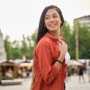 Carefree young woman with long braids smiles while walking through a city square during summer